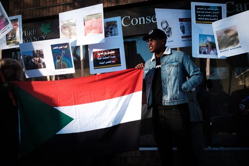 Daniel Crump / Winnipeg Free Press
 Abdalla Ali (right) holds a Sudanese flag as he takes part in a protest outside MP Jim Carrs office (611 Corydon Ave.) in solidarity with the recent protests in Sudan. 
December 28, 2018.