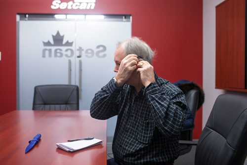 MIKAELA MACKENZIE / WINNIPEG FREE PRESS
Reporter Kevin Rollason puts in earbuds before trying out the SimVoice technology at the Setcan offices in Winnipeg on Friday, Feb. 15, 2019.
Winnipeg Free Press 2019.