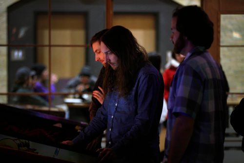 PHIL HOSSACK / WINNIPEG FREE PRESS - Cody Edwards (centre) plays as Landon Butterworth (right) and Morgan Epp (left) watch the shared game at a  Pinball Popup Friday night at the Forks See Declan's story re:Pinball Popup. January 8, 2019.