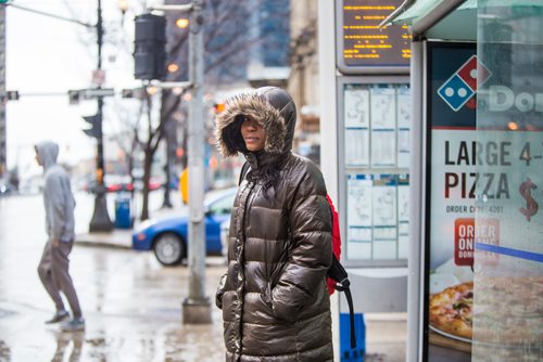 MIKAELA MACKENZIE/WINNIPEG FREE PRESS
Esomchukwu Esther waits for the bus in a parka on Main Street in Winnipeg on Monday, April 15, 2019. 
Winnipeg Free Press 2019