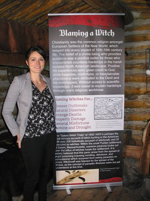 Canstar Community News May  7, 2019 - Fort la Reine executive director Madison Connelly is shown in the musuem's Trapper's Cabin with one of the panels that are part of the musuem's Witchcraft Explored exhibition on until Nov. 15. (ANDREA GEARY/CANSTAR COMMUNITY NEWS)