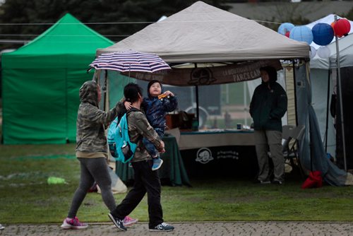 PHIL HOSSACK / WINNIPEG FREE PRESS - 5 yr old Em peers out from his father Bogs Catabay's shoulder as his mother holds the umbrella at the Night Market. What patrons braved the windy drizzle Friday evening stayed under umbrellas as the annual Night Market opened at the Forks. Warmer Sunnier weather is on the way for the weekend. - May24, 2019.