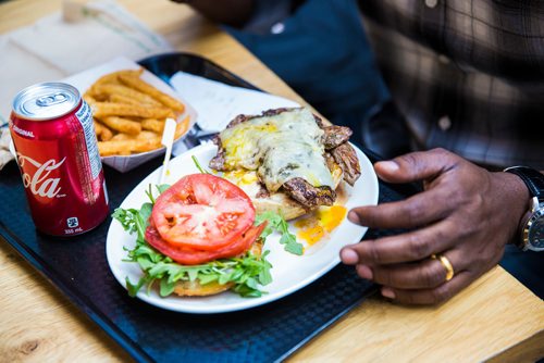 MIKAELA MACKENZIE / WINNIPEG FREE PRESS
Jude Asainayagam enjoys a cheeseburger on a ceramic plate at The Forks in Winnipeg on Tuesday, June 11, 2019.  The Forks recently replaced dishware with 100% reusable and compostable products in its path towards a zero-waste goal. For Tessa Vanderhart story.  
Winnipeg Free Press 2019.