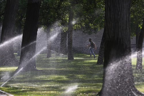 MIKE DEAL / WINNIPEG FREE PRESS
Sprinklers on the grounds of the Manitoba Legislative building forces brave morning foot traffic to sprint a few yards as they head downtown. 
190621 - Friday, June 21, 2019