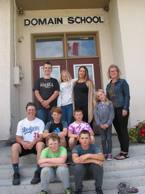 Canstar Community News June 17, 2019 - Domain School's staff and students are shown at the door of the school that will close as of June 28. (Front row, from left) Casey and Elie; (middle row, from left) Brett, Quinn and Alex; (back row, from left) Nathan, Laine, teaching principal Kristen Harley, secretary Sandra Friesen, and Nevaeh. (ANDREA GEARY/CANSTAR COMMUNITY NEWS)
