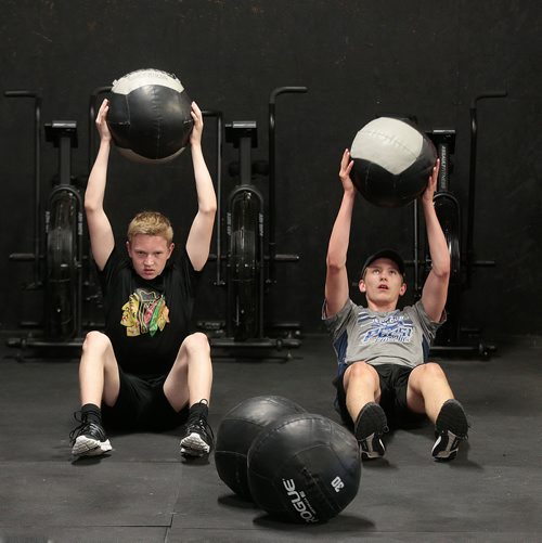 PHIL HOSSACK / WINNIPEG FREE PRESS - Cole Younger (grey shirt) and Easton Lewicki (black shirt) do sit ups while lifting medicine balls at the Cross Fit 204 Gym Wednesday evening. The 15 yr old teenagers are part of a summer fitness program. See Sabrina Carnevale story.  - July 3, 2019.