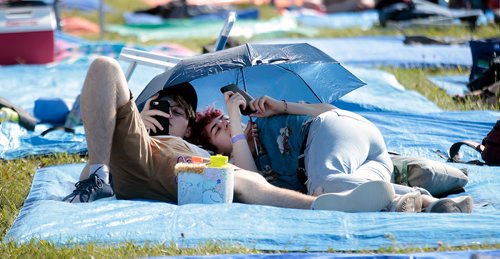 PHIL HOSSACK / WINNIPEG FREE PRESS - Folk Festival- Festival goers secure their tarp and seek shelter from the suns radiation while texting in front of the main stage Friday afternoon.- July 11, 2019.