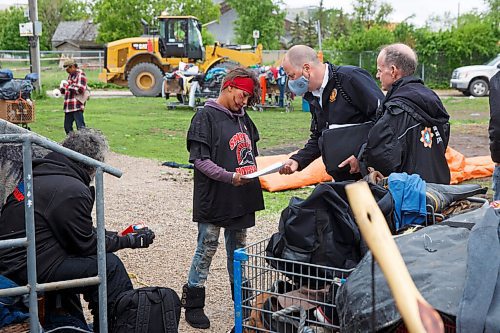 MIKE DEAL / WINNIPEG FREE PRESS
Cleanup of the Point Douglas homeless encampments begins Wednesday morning. People sort through mounds of belongings prior to city crews arrival with a frontend loader and a large truck to remove left over garbage. 
Mark Reshaur Asst. Chief of the Winnipeg Fire Paramedic Service hands Desirae Whitehead a pamphlet detailing the order to vacate the homeless camp by Friday while Rick Lees with the Main Street Project looks on.
200610 - Wednesday, June 10, 2020.