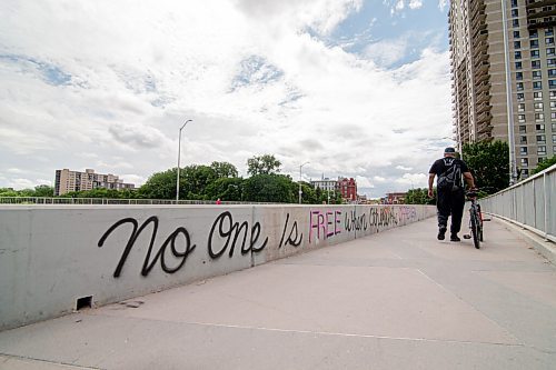 Mike Sudoma / Winnipeg Free Press
A man walks his bike past a graffiti tag reading No One is Free When Others Are Oppressed on the side of the pedestrian walkways along the Osborne Bridge Saturday morning. 
June 20, 2020