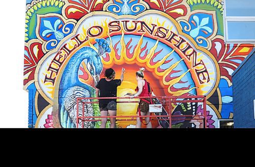 RUTH BONNEVILLE / WINNIPEG FREE PRESS

Standup - New,  Hello Sunshine mural in St James.

Artists Jen Mosienko, (in black) and Elan Beveridge work on finishing their mural on the west wall of 1854 Portage Ave. on Thursday morning.  

Jen Mosienko was the mural  artist who painted the ox carts mural in 1999 which said "Welcome to St. James Village" on it. 

She said that projects like this could not be possible without the support and funding through the St James Biz, Take Pride Winnipeg and Herc Rentals. Also a special thanks to Vandenbergs for allowing us to work on their newly landscaped frontage.

Quote from Jen Mosienko of Jen Mosienko Design, below.

"The original was my very first project, 21 years ago, so this was definitely a bit of a nostalgic project.  I contacted the Biz in the spring and mentioned that I would love the opportunity to give the wall some new life.  In light of past world events and the ongoing Pandemic, I really wanted to do something fun, Non political, Bright and positive for the community.  Everything in the mural represents positivity, wholeness, prosperity and an sense of well being. So hence Hello Sunshine greeting individuals in Sunny St. James."

Note: A Submitted photo of the original ox cart mural that Jen painted is in merlin. 

 Aug 20th, 2020