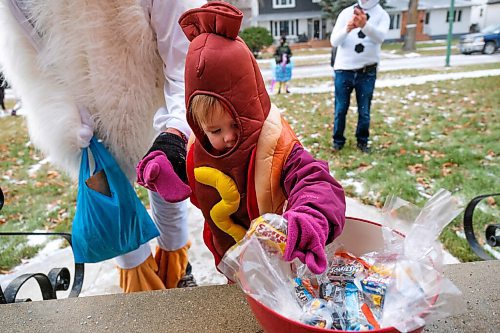 Daniel Crump / Winnipeg Free Press. Violet Moffat, 2, dressed as a hotdog takes a prepackaged bag of candy from a bowl on the doorstep of an Elm Street house. The neighbours on this River Heights block organized a special COVID safe trick-or-treat event so their kids could still enjoy a somewhat normal halloween despite the ongoing pandemic. October 31, 2020.