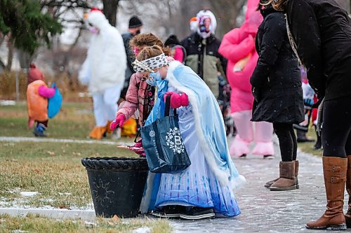 Daniel Crump / Winnipeg Free Press. Madison Dragner, dressed in an Elsa costume, takes a treat from a bucket set on they sidewalk during a special COVID safe halloween event on Elm Street. October 31, 2020.