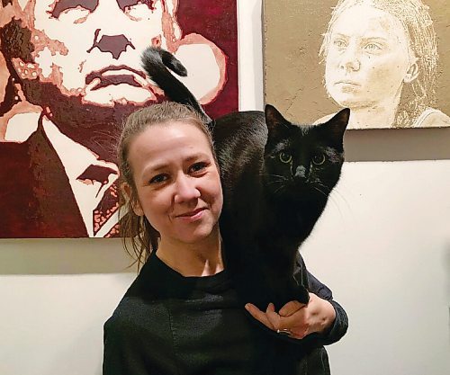 Canstar Community News West End artist Geneviève Levasseur poses with her cat, Gurly, in front of her portraits of Donald Trump and Greta Thunberg.