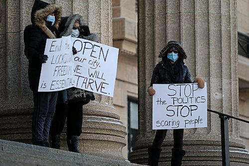 Daniel Crump / Winnipeg Free Press. Three people hold signs as a small group of anti-mask protestors gather at the Manitoba Legislature. November 21, 2020.