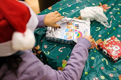 Daniel Crump / Winnipeg Free Press. A child at the Rossbrook House childcare program unwraps a Christmas present as part of a game. Because of the pandemic the childcare program is coming up with creative ways to do Christmas differently this year. December 16, 2020.