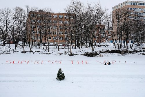 Daniel Crump / Winnipeg Free Press. Members of the community activist group Community Not Cuts write a message that reads suppress the virus in large letters on the bank of the Assiniboine River across from the Manitoba Legislature. January 23, 2021.