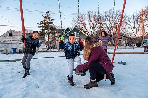 Daniel Crump / Winnipeg Free Press. Sophie Freyet-Agossa puts her youngest son Mathéos boots back on after they came loose while her kids play on the swings in the park across from their St. Boniface home. February 27, 2021.