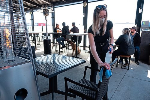 Daniel Crump / Winnipeg Free Press. Jasmine Brown disinfects the table and chairs in preparation for seating guests on the patio at Fionns on Grant Avenue. March 13, 2021.