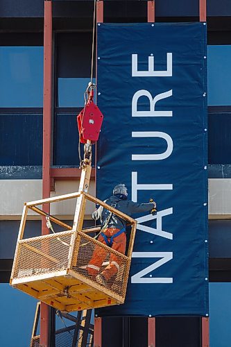 MIKE DEAL / WINNIPEG FREE PRESS
Pete Babiuk with Red River Signs attaches one of three large banners to the side of The Manitoba Museum Monday morning. 
210322 - Monday, March 22, 2021.