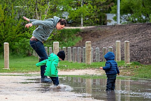 Daniel Crump / Winnipeg Free Press. Andrew McPhail (left)  and 3-year-old Charlie McPhail jump into a puddle as 1.5-year-old Gil McPhail (right) looks on. The McPhail family is making the best of current public health restrictions and wet weekend weather by taking their kids to the park. May 19, 2021.