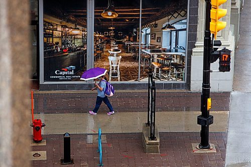 MIKE DEAL / WINNIPEG FREE PRESS
A wet Portage Avenue sidewalk gleams while an umbrella toting pedestrian walks towards their destination Wednesday afternoon.
210609 - Wednesday, June 09, 2021.