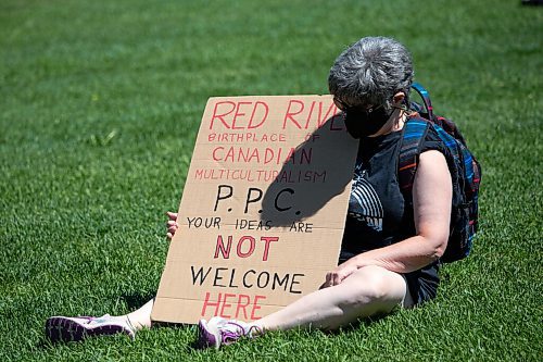 Daniel Crump / Winnipeg Free Press. A counter protestor sits in the grass at the Forks during an anti-restrictions rally Saturday afternoon. June 12, 2021.