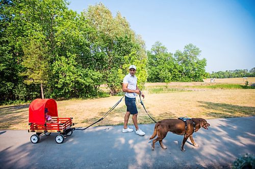 MIKAELA MACKENZIE / WINNIPEG FREE PRESS

Gordon Templeton and his dog, Nala, demonstrate the dog restraint and leash system while pulling Naomi Templeton (two) in a wagon at King's Park in Winnipeg on Friday, July 16, 2021. For Dave Sanderson story.
Winnipeg Free Press 2021.