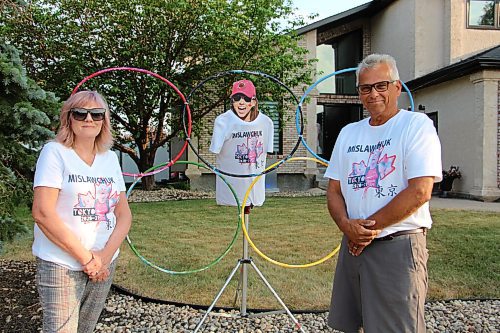 Canstar Community News Eleanor Mislawchuk, left, and her husband Fred pose with the Olympic rings set up they've made in their front yard. Their daughter Madison couldn't attend the July 15 photo shoot; the Mislawchuks stuck a cut-out of her head on a tripod so she could still be there. Eleanor brings cut-outs of Madison and Fred and uses them to cheer Tyler on at his races when the whole family can't make it. (GABRIELLE PICHÉ/CANSTAR COMMUNITY NEWS/HEADLINER)