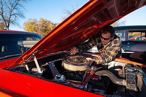 Daniel Crump / Winnipeg Free Press. Matt Knysh makes and adjustment to his orange 1970 Ford Mustang while meeting up with friends at a parking lot by the zoo for a late fall cruise night. October 16, 2021.