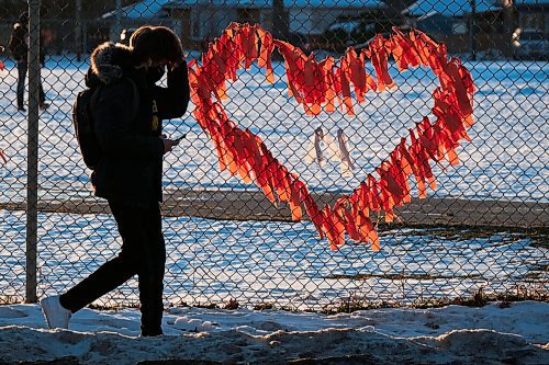 MIKE DEAL / WINNIPEG FREE PRESS
Late afternoon sunlight illuminates orange ribbons on the schoolyard fence at Kelvin High School just as classes are dismissed for the day. The ribbons are a memorial to the unmarked graves at a former residential schools that were discovered this year across the country. 
211214 - Tuesday, December 14, 2021.