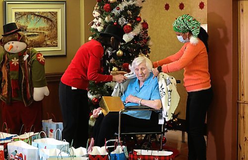 RUTH BONNEVILLE / WINNIPEG FREE PRESS
Local - Convalescent Home Feature
Convalescent Home of Winnipeg resident, Mildred Giesbrecht, 105 years old, enjoys opening her gifts from the home presented to her by staff, Sherry Heppner, development coordinator (red), and Kiran Benipal recreation manager (orange), in front of their Christmas tree in the home's foyer this week.
One of the gifts given to residents was a shawl which the staff tried on Mildred after it was opened.
Photos for Christmas feature on how this PCH is adapting to their second pandemic Christmas. Sherry with gifts.
Dec 21st, 2021