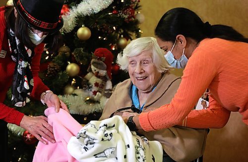 RUTH BONNEVILLE / WINNIPEG FREE PRESS
Local - Convalescent Home Feature
Convalescent Home of Winnipeg resident, Mildred Giesbrecht, 105 years old, enjoys opening her gifts from the home presented to her by staff, Sherry Heppner, development coordinator (red), and Kiran Benipal recreation manager (orange), in front of their Christmas tree in the home's foyer this week.
One of the gifts given to residents was a shawl which the staff tried on Mildred after it was opened.
Photos for Christmas feature on how this PCH is adapting to their second pandemic Christmas. Sherry with gifts.
Dec 21st, 2021