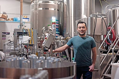 Canstar Community News Sean Shoyoqubov, owner of Oxus Brewing Company, stands amid beer vats and the canning machine, as he and an employee prepare a fresh batch for distribution.