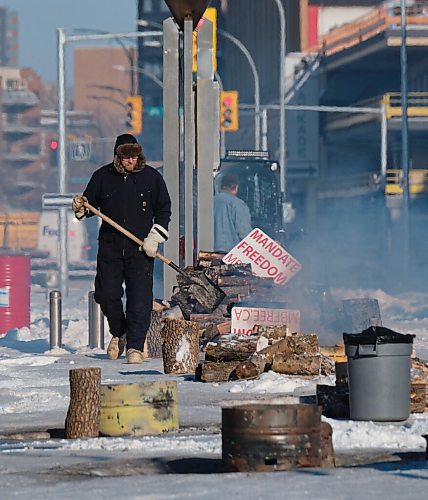 MIKE DEAL / WINNIPEG FREE PRESS
A protester cleans up the fire pits early Monday morning that have sprouted up along Memorial Boulevard. They continue to block the entrance to the Manitoba Legislative building on Broadway early Monday morning. The mandate protesters, who have been set up along Memorial Boulevard since Friday morning, now have access to portable toilets and are using fire pits to keep warm.
220207 - Monday, February 07, 2022.