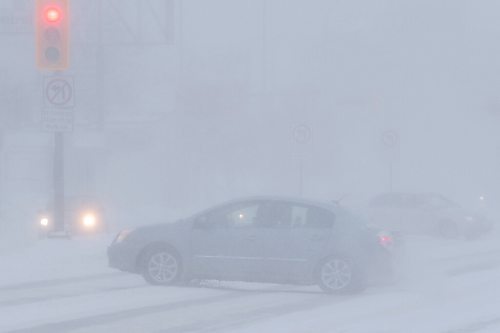 Daniel Crump / Winnipeg Free Press. A car crosses Portage Ave. Saturday afternoon as a blizzard reduces visibility significantly. February 19, 2022.