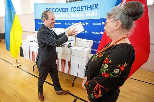MIKE DEAL / WINNIPEG FREE PRESS
Finance Minister Cameron Friesen during the traditional Budget 2022 shoe announcement where he is handing a box of essential personal hygiene items to Joanne Lewandosky, president of the Ukrainian Canadian Congress, at 935 Main Street, Ukrainian National Federation of Canada, Monday morning.
220411 - Monday, April 11, 2022.