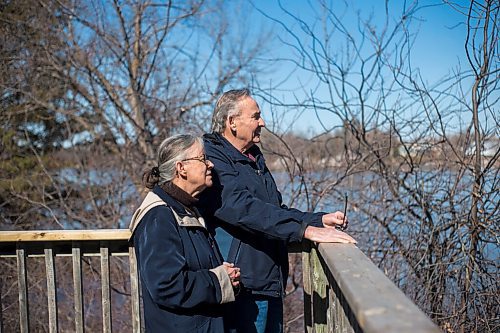 MIKAELA MACKENZIE / WINNIPEG FREE PRESS

Bob and Judy Roehle, St. Norbert homeowners who shared their memories of the 1997 flood, pose for a portrait by the river on the deck that Bob tied to a tree to keep the house from floating away (which has since been rebuilt significantly higher) on their property on Tuesday, April 26, 2022.
Winnipeg Free Press 2022.