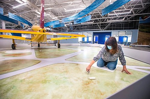 MIKAELA MACKENZIE / WINNIPEG FREE PRESS

Artist Estelle Régnier puts a clear coat onto a floor mural underneath the Musketeer plane at the new Royal Aviation Museum of Western Canada in Winnipeg on Wednesday, May 11, 2022. For Al Small story.
Winnipeg Free Press 2022.