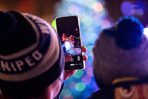Daniel Crump / Winnipeg Free Press. Leo Soriano uses his phone to take a photo of Santa during the 2021 Santa Clause Parade at Shaw Park in Winnipeg. This year the parade remained stationary while families were able to walk up to Santas float to get a selfie with Santa. November 20, 2021.