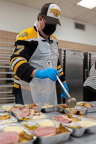 Gord Robbins add gravy to Westman and Area Traditional Christmas Dinner deliveries Saturday at Crocus Plains Regional Secondary School. (Chelsea Kemp/The Brandon Sun)