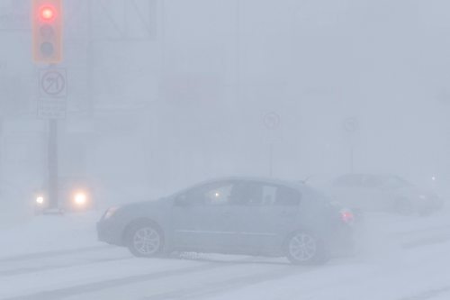 Daniel Crump / Winnipeg Free Press. A car crosses Portage Ave. Saturday afternoon as a blizzard reduces visibility significantly. February 19, 2022.