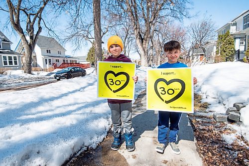 Mike Sudoma / Winnipeg Free Press
Brothers Owen (left) and Max Walker (right) hold up signs in support of 30 km/h speed limits in residential zones Thursday afternoon. 
March 31, 2022