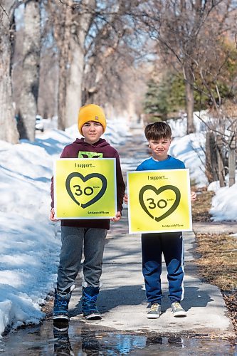 Mike Sudoma / Winnipeg Free Press
Brothers Owen (left) and Max Walker (right) hold up signs in support of 30 km/h speed limits in residential zones Thursday afternoon. 
March 31, 2022