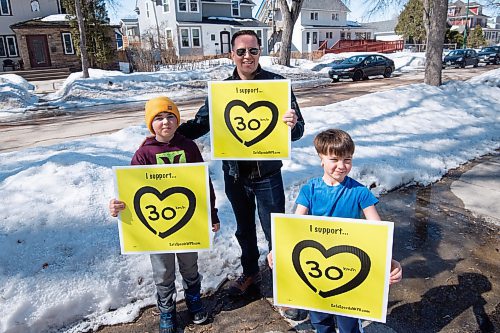 Mike Sudoma / Winnipeg Free Press
Ian Walker hold up signs with his two sons, Owen (left) and Max (right) in support of 30 km/h speed limits in residential zones Thursday afternoon. 
March 31, 2022