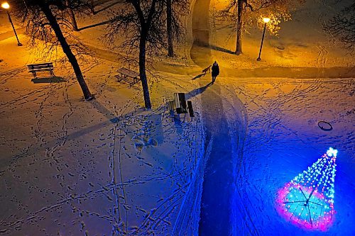 Footprints dot the snow and a woman walks a dog through Stanley Park in Brandon under the glow of lamps and Christmas lights on a mild Monday evening. (Tim Smith/The Brandon Sun)