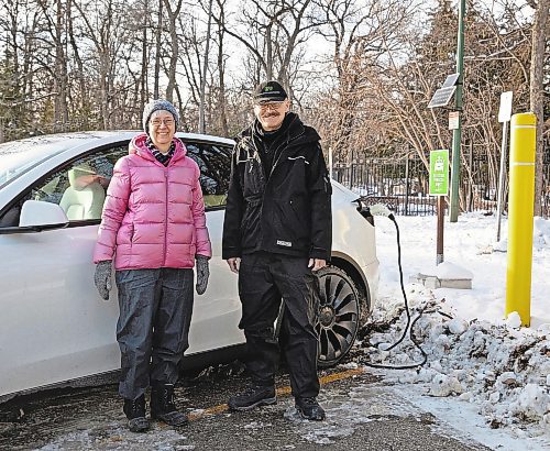 Robert Elms (in black) and his wife, Lois, are photographed with their Tesla at Assiniboine Park on November 21, 2022. (Jessica Lee/Winnipeg Free Press)