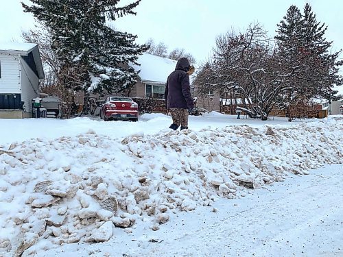 Mary Anne Fendick stands beside the snowbank left behind when a city grader plowed her street on Sunday, trapping her car in her driveway. (Matt Goerzen/The Brandon Sun)