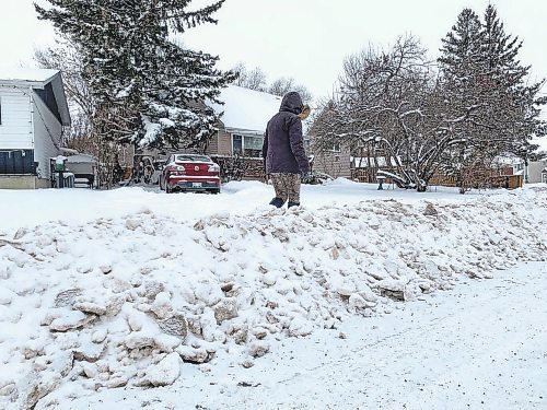 Mary Anne Fendick stands beside the snowbank left behind when a city grader plowed her street on Sunday, trapping her car in her driveway. (Matt Goerzen/The Brandon Sun)