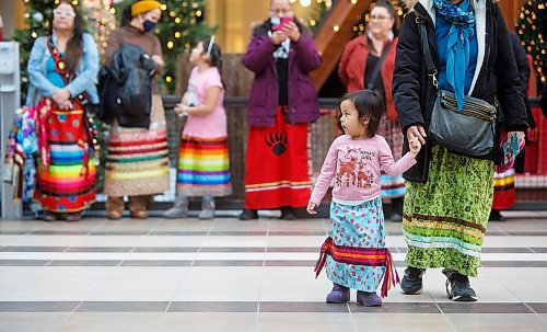 MIKE DEAL / WINNIPEG FREE PRESS
Wabigwan Greene, almost 3-yrs-old, holds her grandmother's hand during the first National Ribbon Skirt Day event at the Polo Park Shopping Centre on Wednesday. National Ribbon Skirt Day is held on January 4th a day where Indigenous women across the country are encouraged to wear their traditional regalia to celebrate their culture, their strength and their connection as women.
230104 - Wednesday, January 04, 2023.