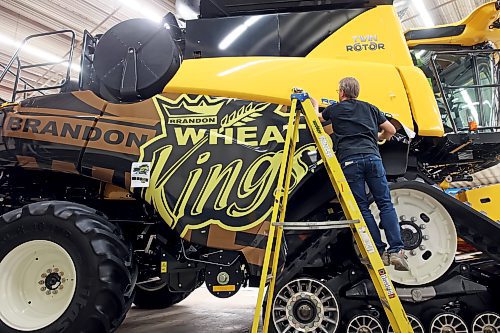 Owner Al Grebinski with Accent Striping and Lettering affixes a Brandon Wheat Kings wrap to a New Holland combine at the Keystone Centre on Monday in preparation for Manitoba Ag Days 2023, which begins today. See more photos on Page A3. (Tim Smith/The Brandon Sun)